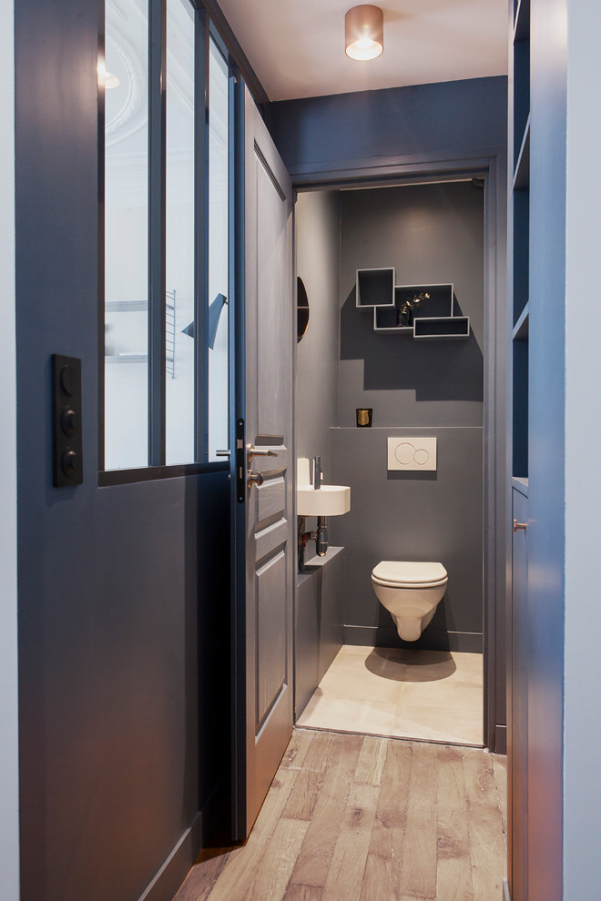 Idéer för små minimalistiska toaletter, med en vägghängd toalettstol, blå väggar, ljust trägolv och ett väggmonterat handfat