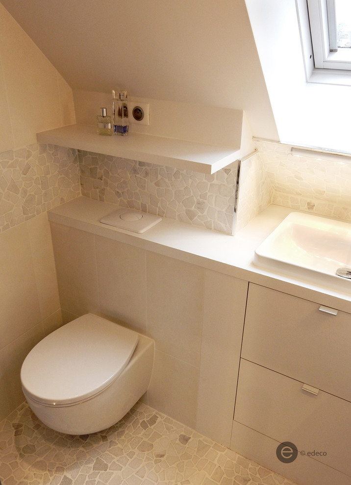 Design ideas for a small contemporary cloakroom in Paris with recessed-panel cabinets, white cabinets, a wall mounted toilet, white tiles, pebble tiles, white walls, pebble tile flooring, a submerged sink and laminate worktops.