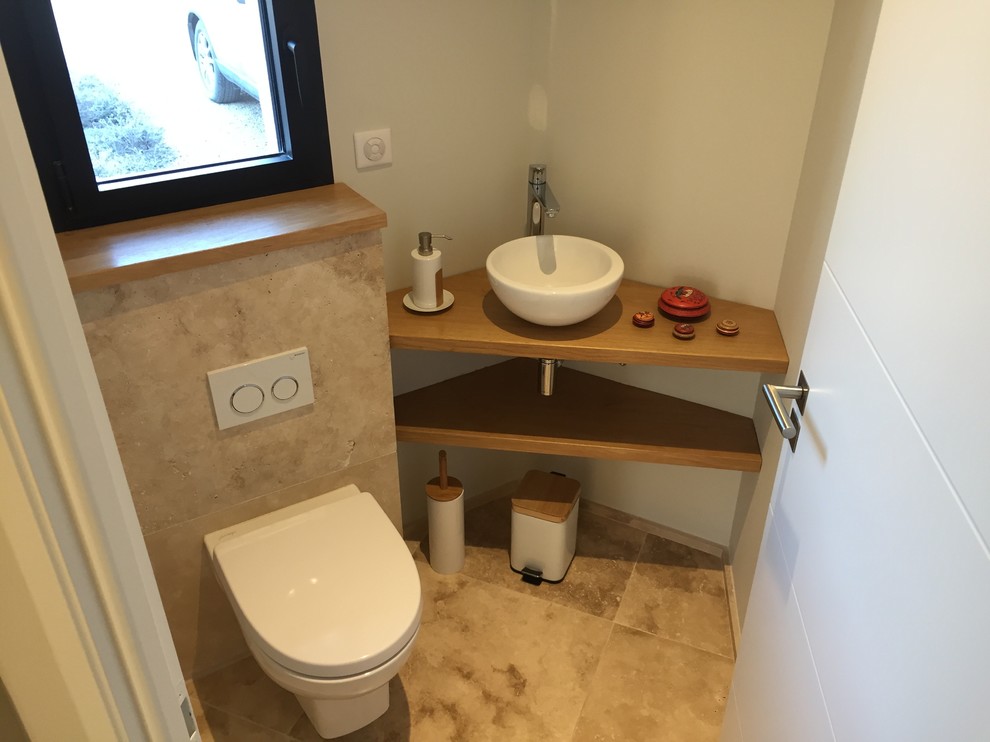Idée de décoration pour un WC suspendu design avec un carrelage beige, du carrelage en travertin, un mur blanc, un sol en travertin, un lavabo posé, un plan de toilette en bois et un sol beige.