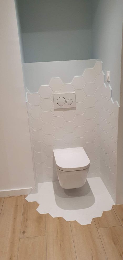 Cette photo montre un WC suspendu chic de taille moyenne avec un carrelage blanc, des carreaux de céramique, un mur blanc et un sol en carrelage imitation parquet.