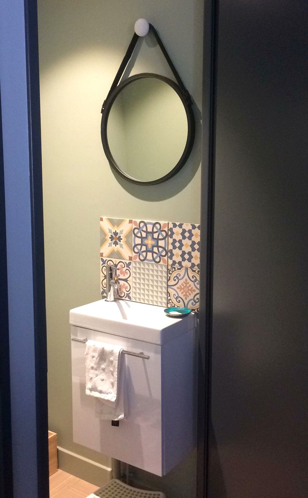 Idée de décoration pour un petit WC suspendu design avec un placard à porte plane, des portes de placard blanches, un carrelage multicolore, des carreaux de béton, un mur vert, un sol en linoléum, un lavabo intégré, un sol beige et un plan de toilette blanc.