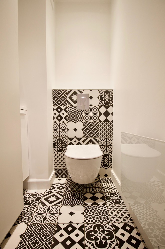 Cette photo montre un petit WC suspendu tendance avec un placard à porte affleurante, des portes de placard blanches, un carrelage noir et blanc, des carreaux de béton, un mur blanc, carreaux de ciment au sol, un lavabo suspendu et un sol multicolore.