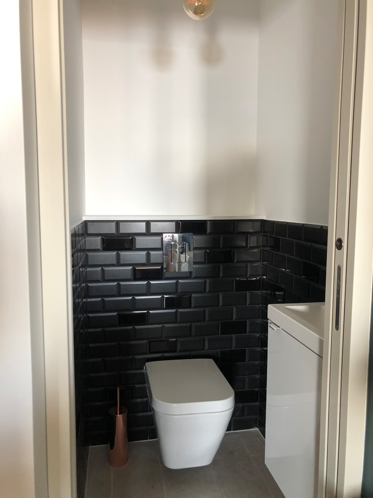 Immagine di un piccolo bagno di servizio minimal con WC sospeso, piastrelle nere, piastrelle diamantate, pareti nere, pavimento con piastrelle in ceramica, lavabo sottopiano, pavimento beige e top bianco