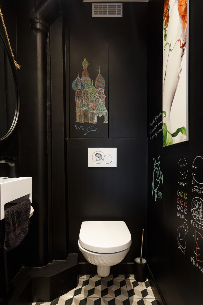 Photo of a small industrial cloakroom in Paris with beaded cabinets, black cabinets, a wall mounted toilet, black tiles, black walls, cement flooring, a wall-mounted sink, solid surface worktops, multi-coloured floors, white worktops and a built in vanity unit.