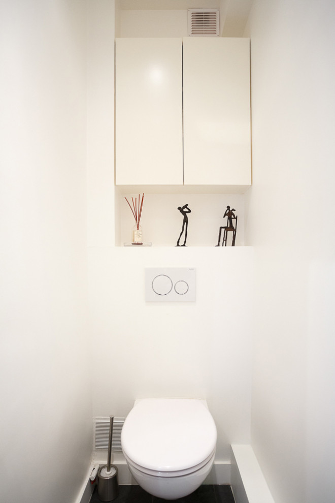 This is an example of a small contemporary cloakroom in Paris with beaded cabinets, white cabinets, a wall mounted toilet, white tiles, metro tiles, white walls, cement flooring, a wall-mounted sink, grey floors, white worktops and a floating vanity unit.