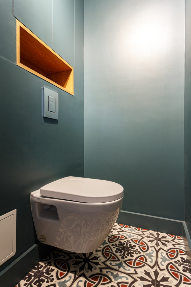 Cette photo montre un petit WC suspendu avec un placard à porte affleurante, des portes de placard bleues, un carrelage bleu, un mur bleu, carreaux de ciment au sol, un plan de toilette en surface solide, un sol multicolore et un plan de toilette blanc.