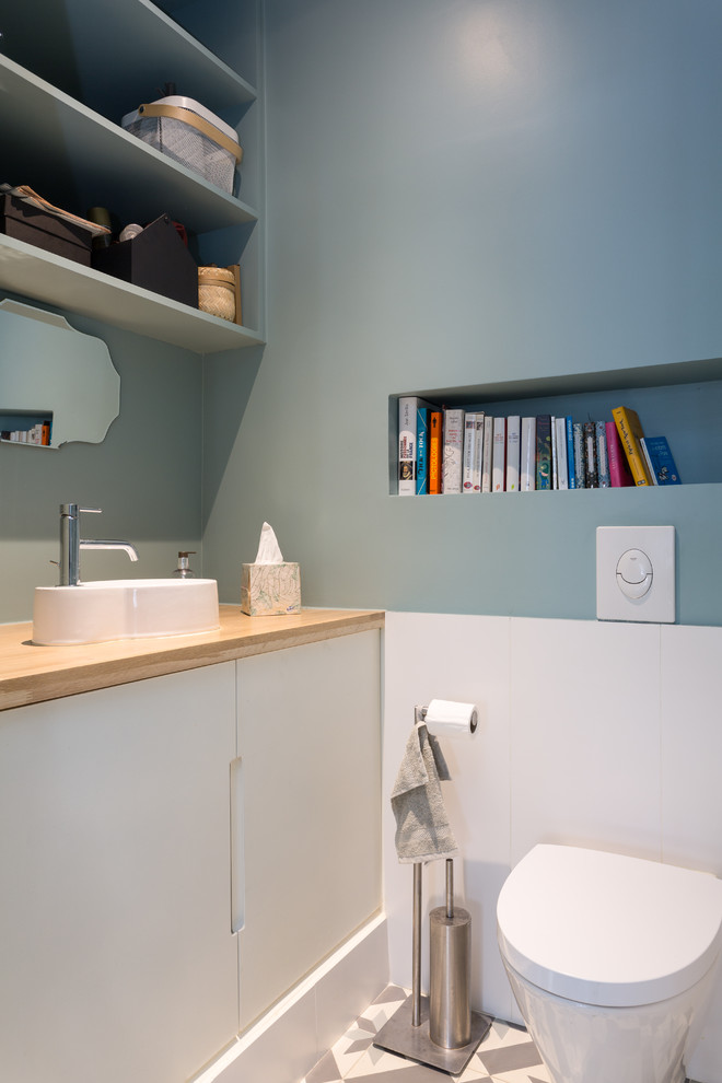 Inspiration för ett mellanstort funkis beige beige toalett, med vita skåp, en vägghängd toalettstol, blå väggar, grått golv, släta luckor, vit kakel, porslinskakel, cementgolv, ett fristående handfat och träbänkskiva