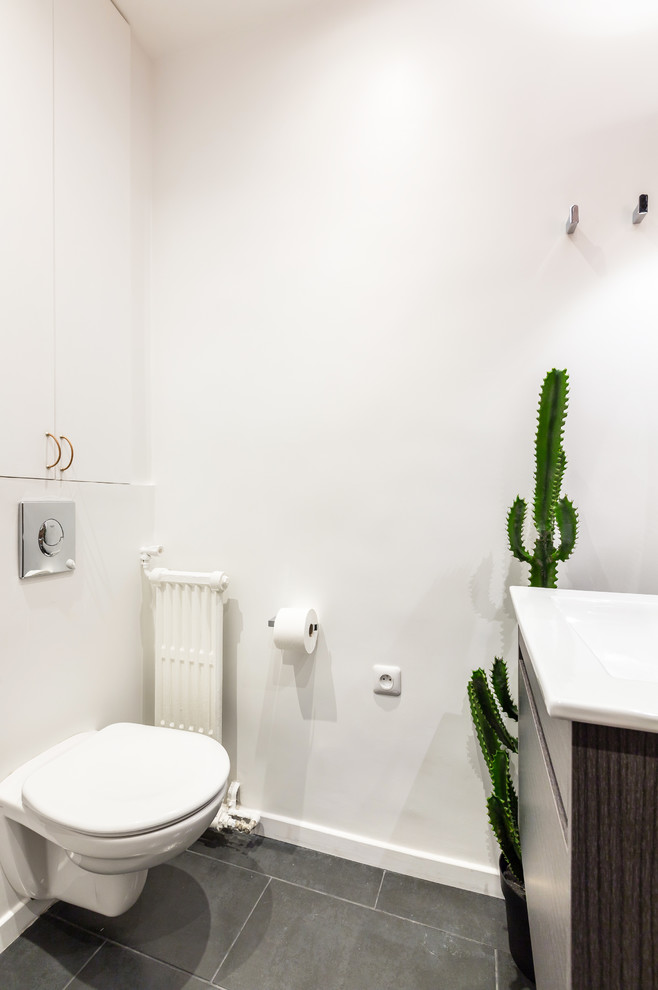 パリにある高級な小さなインダストリアルスタイルのおしゃれなトイレ・洗面所 (フラットパネル扉のキャビネット、白いキャビネット、壁掛け式トイレ、茶色いタイル、セラミックタイル、白い壁、セラミックタイルの床、コンソール型シンク、人工大理石カウンター、黒い床、白い洗面カウンター) の写真