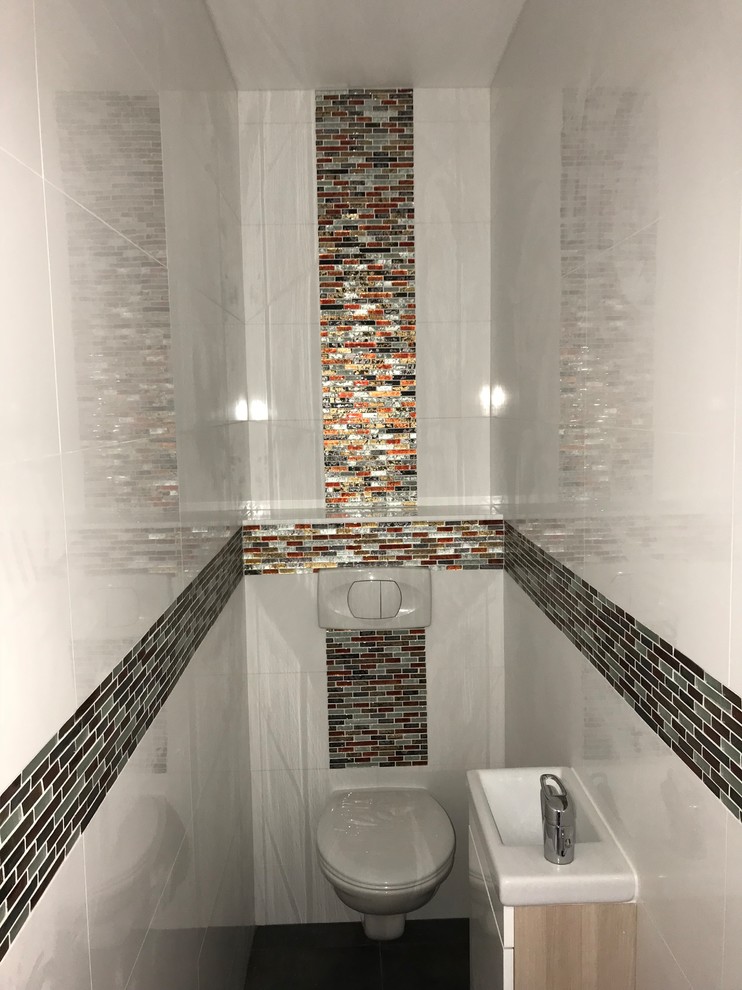Photo of a medium sized modern cloakroom in Paris with beaded cabinets, light wood cabinets, a wall mounted toilet, multi-coloured tiles, porcelain tiles, white walls, ceramic flooring, a wall-mounted sink, tiled worktops, grey floors and multi-coloured worktops.
