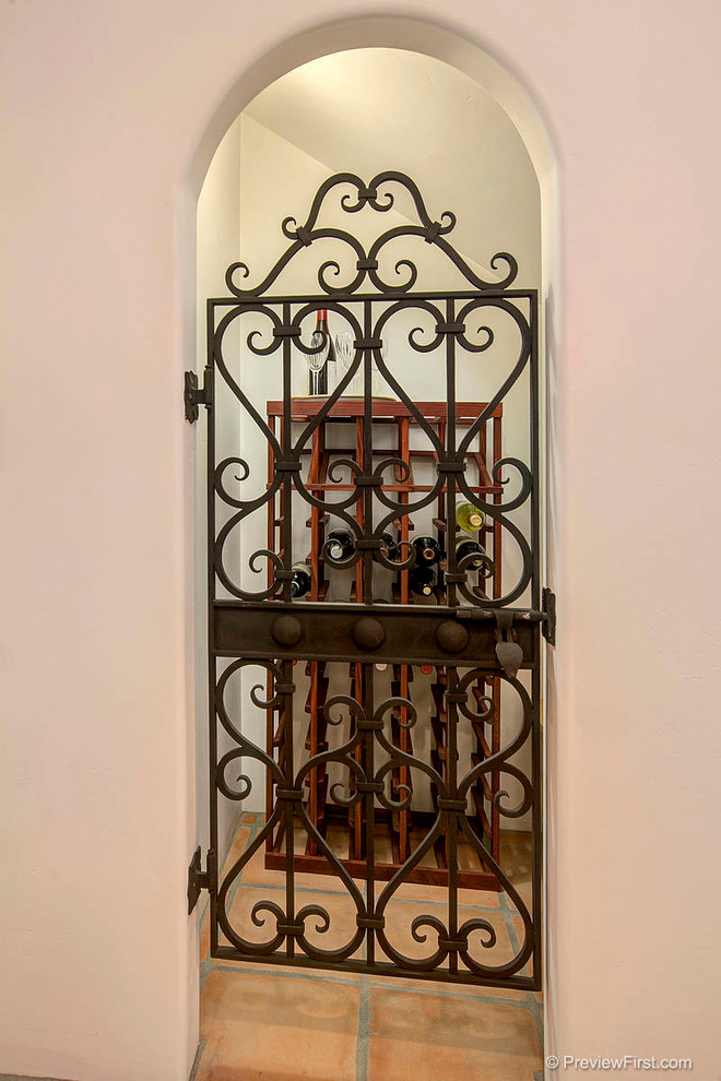 На фото: маленький винный погреб в средиземноморском стиле с полом из терракотовой плитки и витринами для на участке и в саду