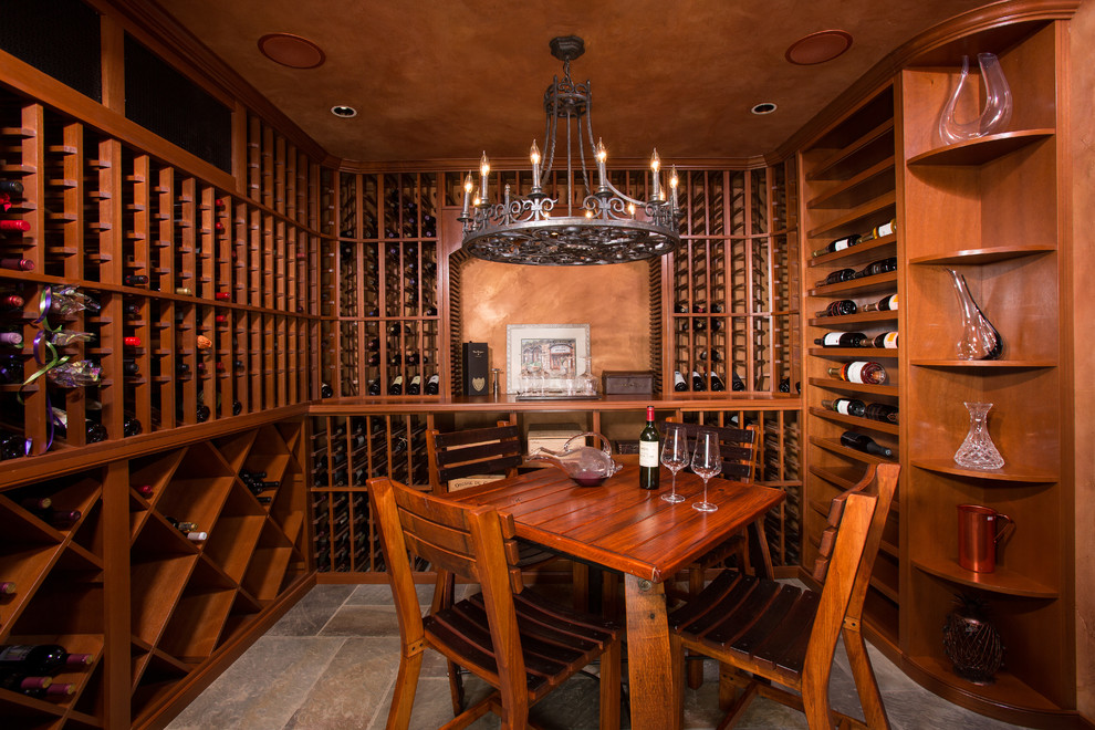 Cette photo montre une grande cave à vin chic avec un sol en ardoise, des casiers et un sol marron.