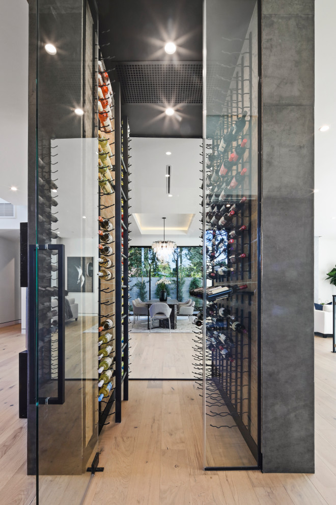 This is an example of a large contemporary wine cellar in Los Angeles with light hardwood flooring, display racks and beige floors.