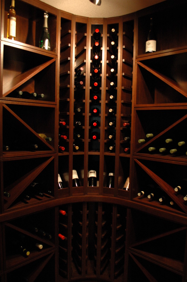 Bild på en mellanstor amerikansk vinkällare, med mellanmörkt trägolv och vinställ med diagonal vinförvaring