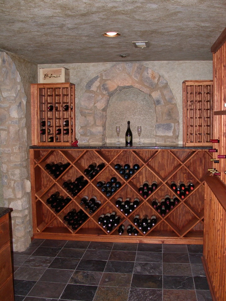Rustik inredning av en stor vinkällare, med skiffergolv, vinställ med diagonal vinförvaring och grått golv