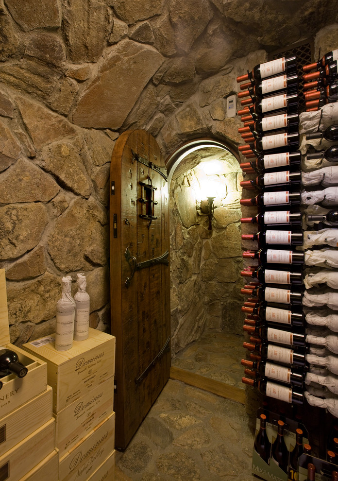 Ejemplo de bodega rústica de tamaño medio con suelo de piedra caliza, botelleros y suelo marrón