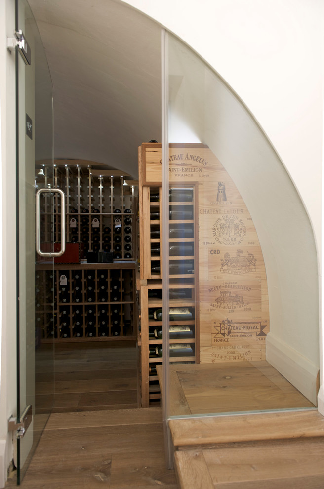 This is an example of a medium sized contemporary wine cellar in London with medium hardwood flooring and display racks.