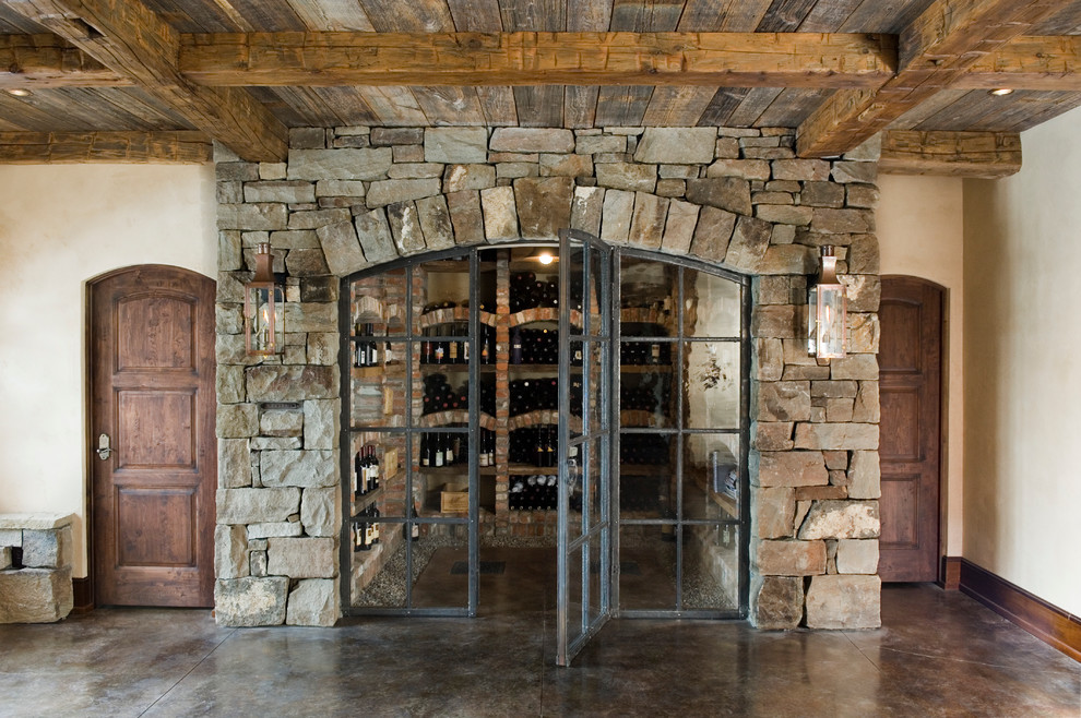Cette photo montre une cave à vin montagne de taille moyenne avec sol en béton ciré, un présentoir et un sol marron.