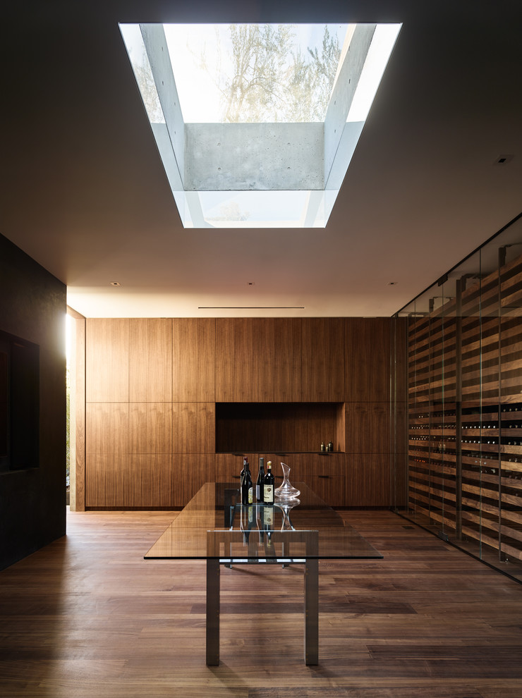 Imagen de bodega minimalista con suelo de madera en tonos medios, botelleros y suelo marrón
