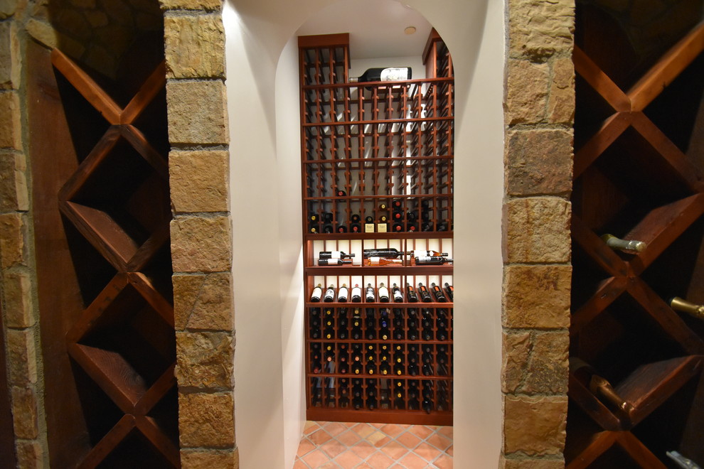 Réalisation d'une cave à vin tradition de taille moyenne avec tomettes au sol, un présentoir et un sol orange.
