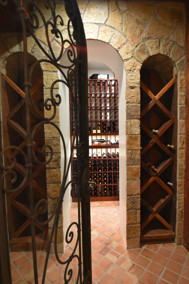 На фото: винный погреб среднего размера в стиле шебби-шик с полом из терракотовой плитки, витринами и оранжевым полом