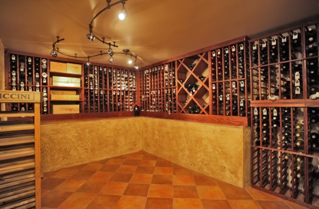Пример оригинального дизайна: большой винный погреб в классическом стиле с полом из керамической плитки, стеллажами и оранжевым полом