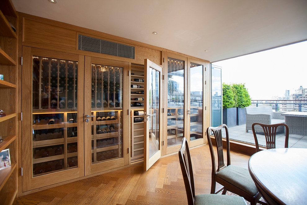 Elegant light wood floor wine cellar photo in London with display racks