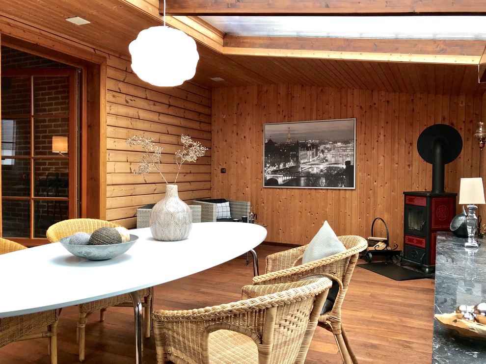 Ejemplo de galería campestre de tamaño medio con suelo de madera en tonos medios, estufa de leña, marco de chimenea de baldosas y/o azulejos, techo de vidrio y suelo marrón