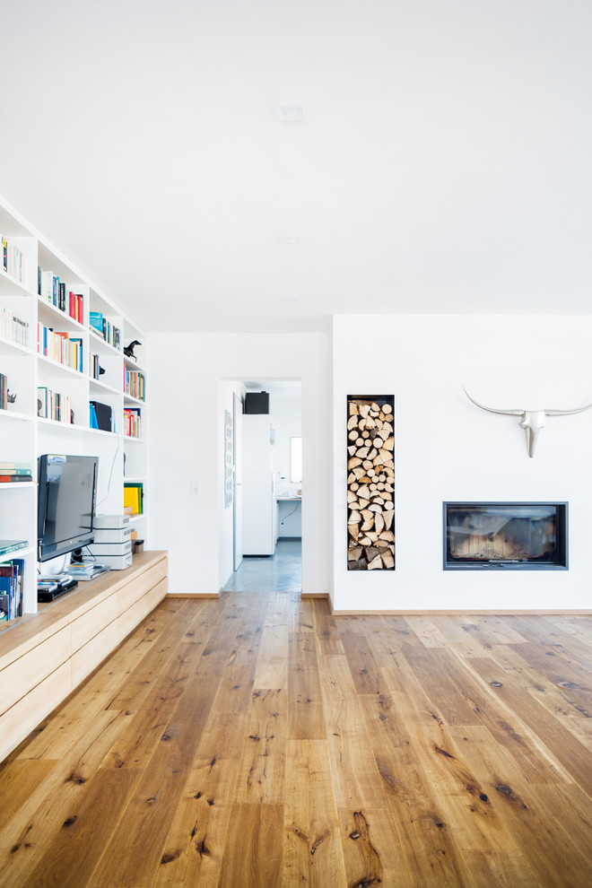 Ejemplo de sala de estar con biblioteca abierta contemporánea de tamaño medio con paredes blancas, estufa de leña, marco de chimenea de yeso, suelo de madera en tonos medios, pared multimedia y suelo marrón