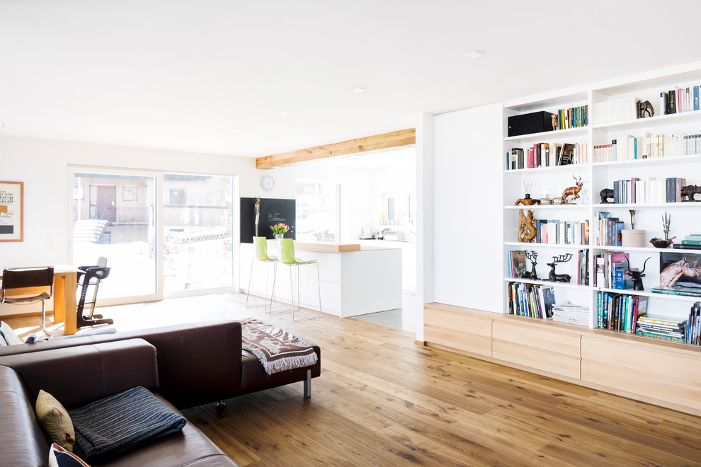 Immagine di un grande soggiorno nordico aperto con libreria, pareti bianche, pavimento in legno massello medio, nessun camino e pavimento marrone