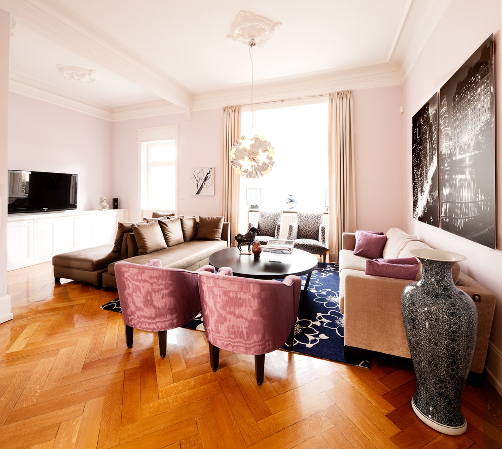 Cette photo montre une grande salle de séjour tendance fermée avec un mur rose, un sol en bois brun, aucune cheminée et un téléviseur fixé au mur.