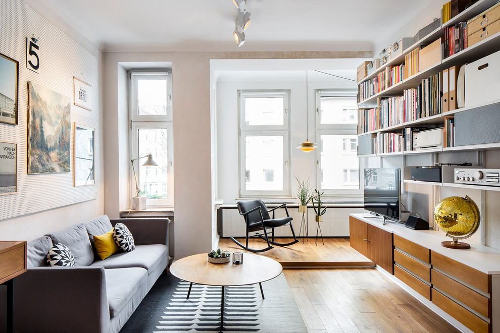 Ejemplo de sala de estar con biblioteca escandinava sin chimenea con paredes blancas, suelo de madera en tonos medios y televisor independiente