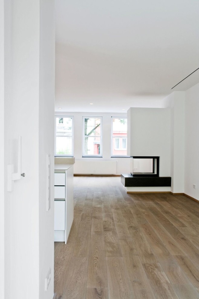 Immagine di un ampio soggiorno minimal con pareti bianche, pavimento in legno verniciato e camino classico