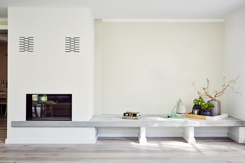 Inspiration för ett minimalistiskt vardagsrum, med vita väggar, ljust trägolv, en bred öppen spis och en spiselkrans i gips