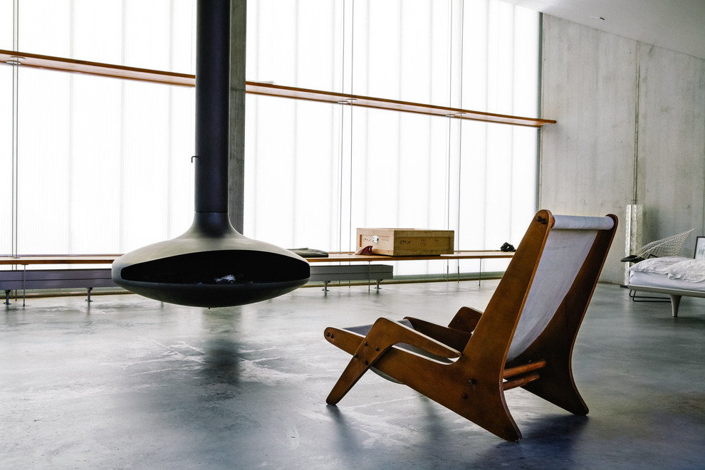 This is an example of a large industrial living room in Berlin with grey walls, concrete flooring and a hanging fireplace.