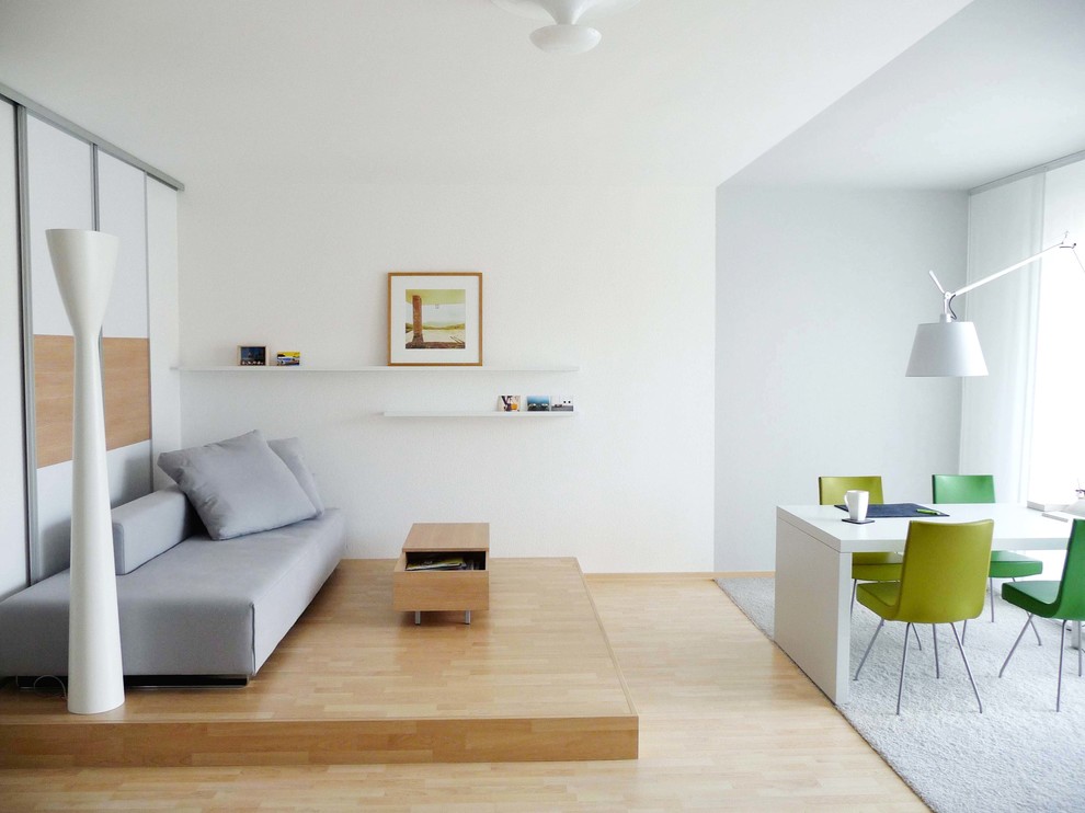 На фото: маленькая открытая гостиная комната в современном стиле с белыми стенами, светлым паркетным полом и ковром на полу без телевизора для на участке и в саду с