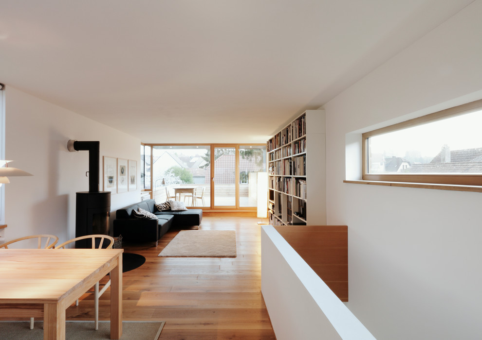 Modelo de sala de estar con biblioteca abierta moderna grande con paredes blancas, suelo de madera en tonos medios y todas las chimeneas
