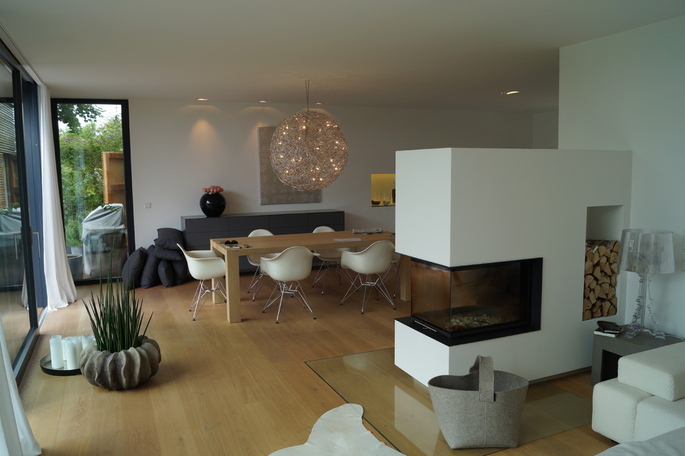 Cette image montre une salle de séjour design de taille moyenne et ouverte avec un mur gris, un sol en bois brun, une cheminée double-face et un manteau de cheminée en plâtre.