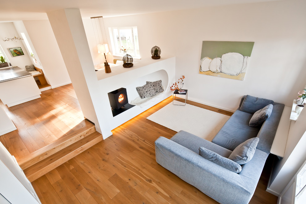 Ejemplo de sala de estar cerrada minimalista con paredes blancas, suelo de madera clara, chimeneas suspendidas, marco de chimenea de yeso y suelo beige