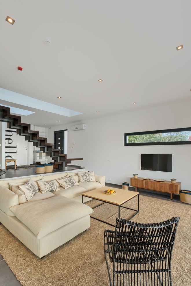Cette image montre une très grande salle de séjour design ouverte avec un mur blanc, un sol en bois brun, une cheminée ribbon, un manteau de cheminée en plâtre, un téléviseur fixé au mur et un sol marron.