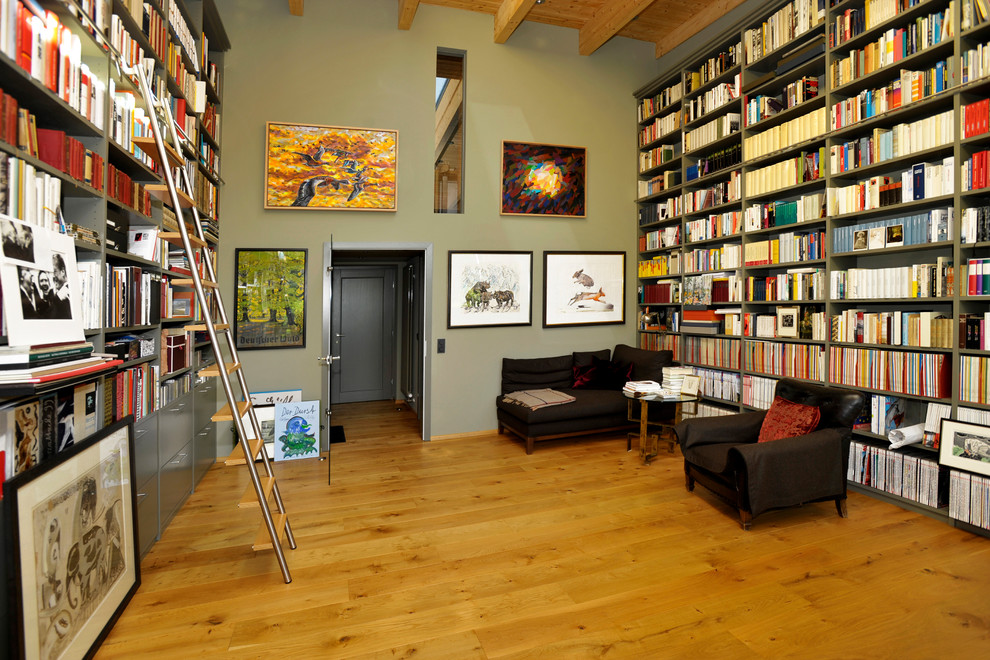 Lantlig inredning av ett mycket stort vardagsrum, med ett bibliotek, gröna väggar och mellanmörkt trägolv