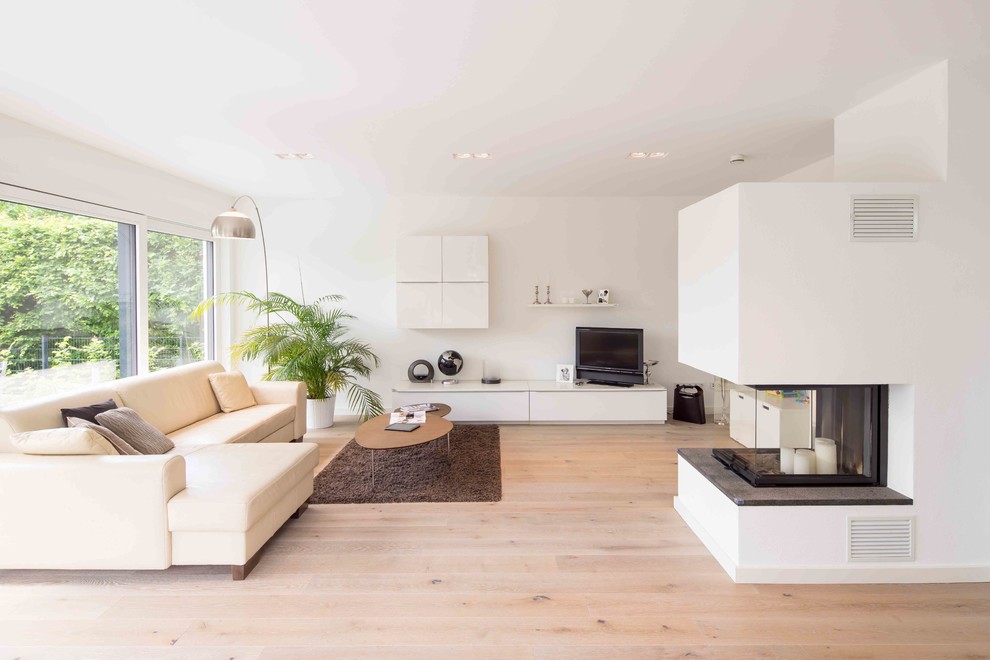 Ejemplo de salón minimalista de tamaño medio con paredes blancas, suelo de madera clara, estufa de leña, marco de chimenea de yeso, televisor independiente y suelo marrón
