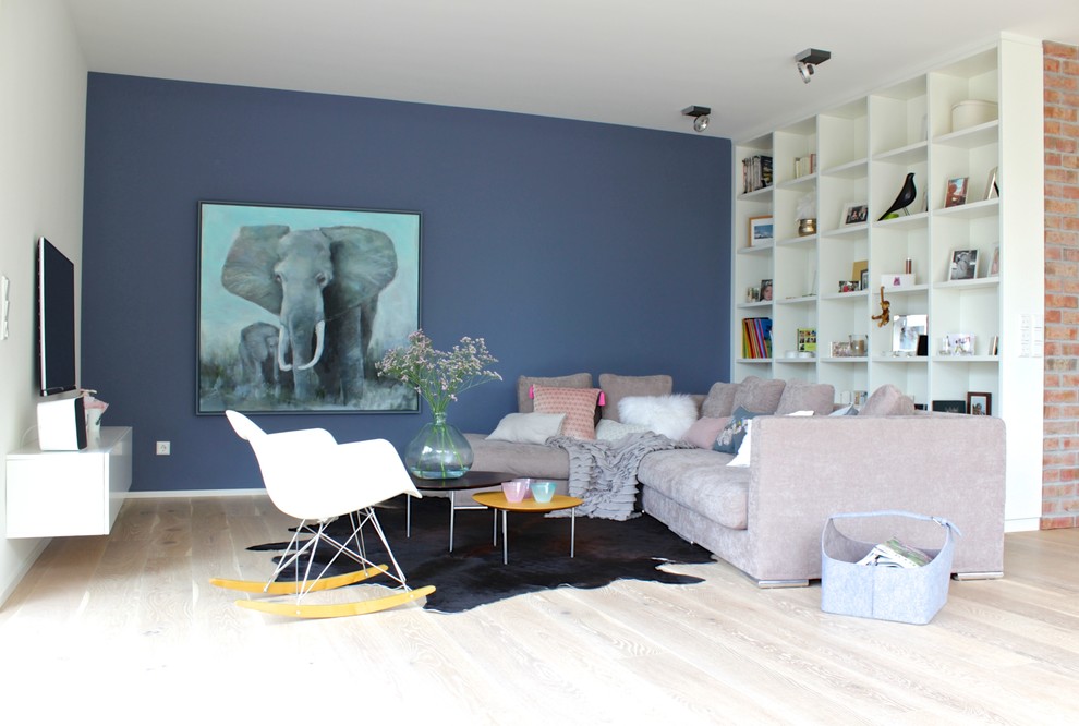 Inspiration pour une grande salle de séjour design ouverte avec un mur bleu, parquet clair, un téléviseur fixé au mur, une bibliothèque ou un coin lecture, aucune cheminée et un sol marron.