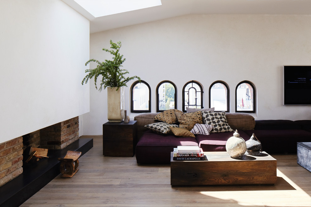 Esempio di un grande soggiorno design con pareti bianche, pavimento in legno massello medio, camino classico e cornice del camino in mattoni