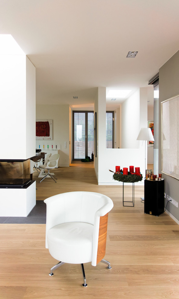Imagen de salón para visitas abierto actual con paredes blancas, suelo de madera clara, chimenea de doble cara y marco de chimenea de yeso