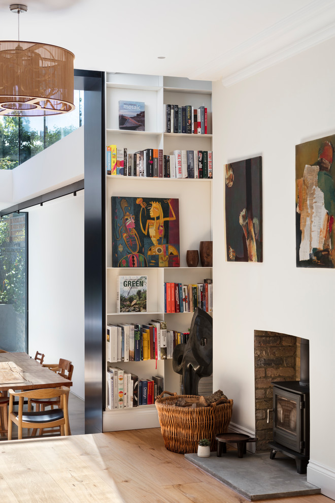 Immagine di un grande soggiorno design aperto con libreria, pareti bianche, parquet chiaro, stufa a legna e cornice del camino in intonaco