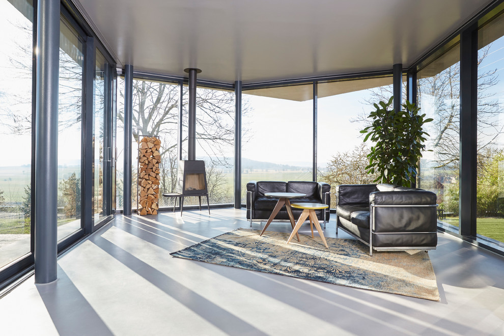 Esempio di un grande soggiorno design aperto con stufa a legna, pavimento in cemento e cornice del camino in metallo