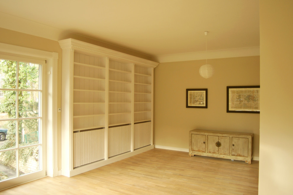 Imagen de sala de estar con biblioteca cerrada campestre de tamaño medio con paredes amarillas, suelo de madera clara y suelo marrón