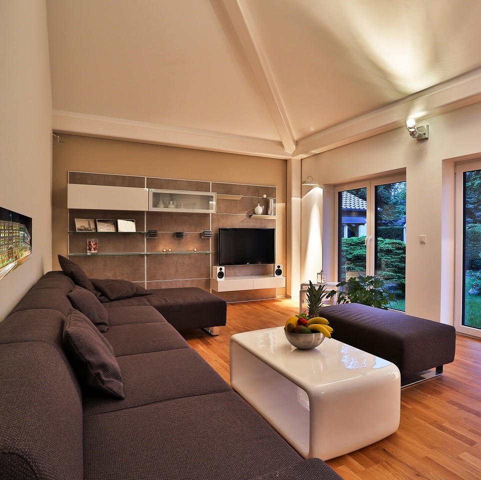На фото: большая открытая гостиная комната в современном стиле с бежевыми стенами, паркетным полом среднего тона, телевизором на стене, коричневым полом, балками на потолке и обоями на стенах без камина с