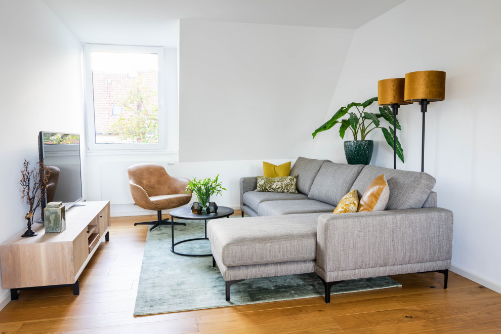 Imagen de salón abierto contemporáneo pequeño con paredes blancas, suelo de madera clara y televisor independiente
