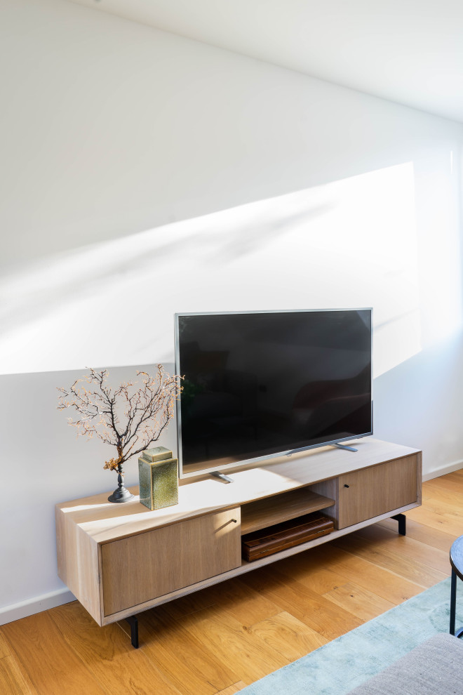 Inredning av ett mellanstort allrum med öppen planlösning, med vita väggar, ljust trägolv och en fristående TV